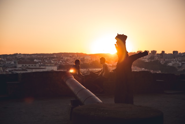 Two people sit on a scenic overlook during sunset, symbolizing quiet, authentic moments in contrast to romanticized ideals.
